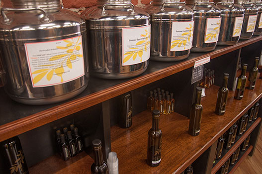 Stainless steel balsamic vinegar tasting containers and bottled olive oils displayed on wooden shelves at D'Olivo Tasting Bar in Walla Walla