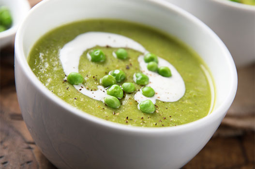 Bowl of creamy spring pea soup topped with crème fraîche and fresh peas on a rustic wood surface
