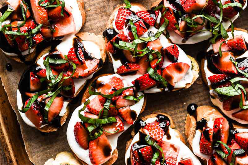 Strawberry balsamic crostini on a wooden board with ricotta and fresh basil